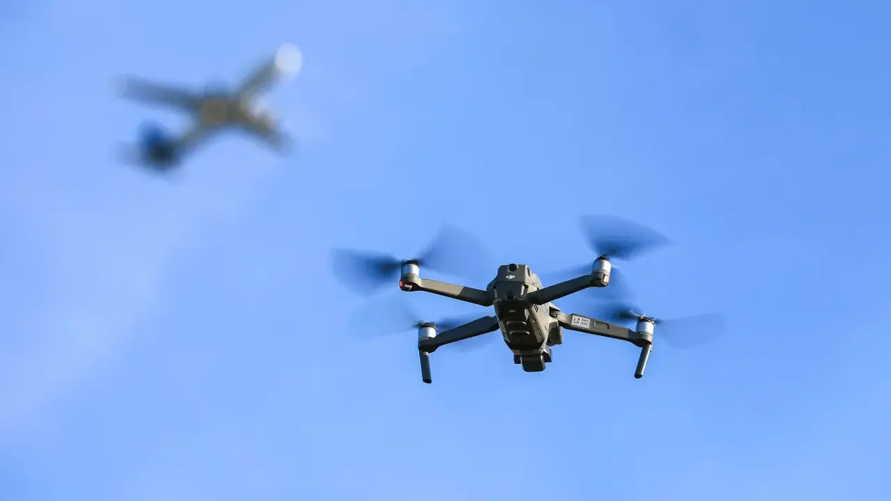 Ein moderner Drohne fliegt im Vordergrund, im Hintergrund ein unscharfes Flugzeug.