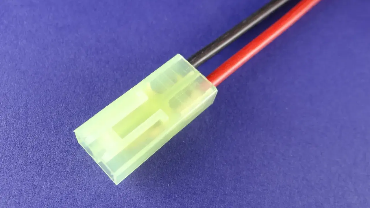 Ein gelber mini Tamiya Stecker mit roten und schwarzen Kabeln auf blauem Hintergrund.