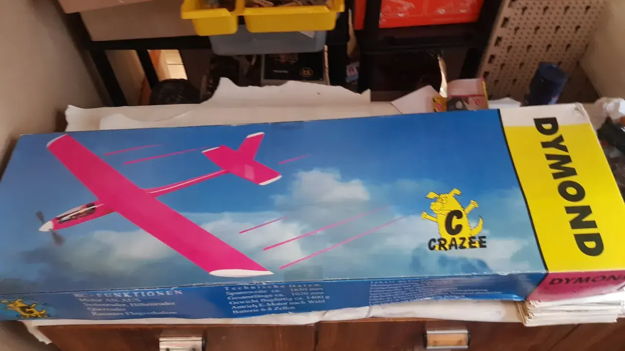 DYMOND RC-Flugzeug-Karton mit pinkem Modell. Ein gelber Streifen mit dem Schriftzug DYMOND.