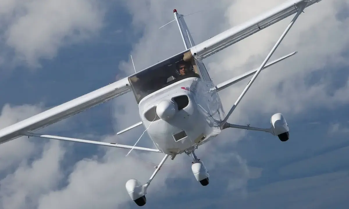 Eine weiße Cessna Skyhawk fliegt durch bewölkten Himmel. Der Pilot blickt aus dem Cockpit.