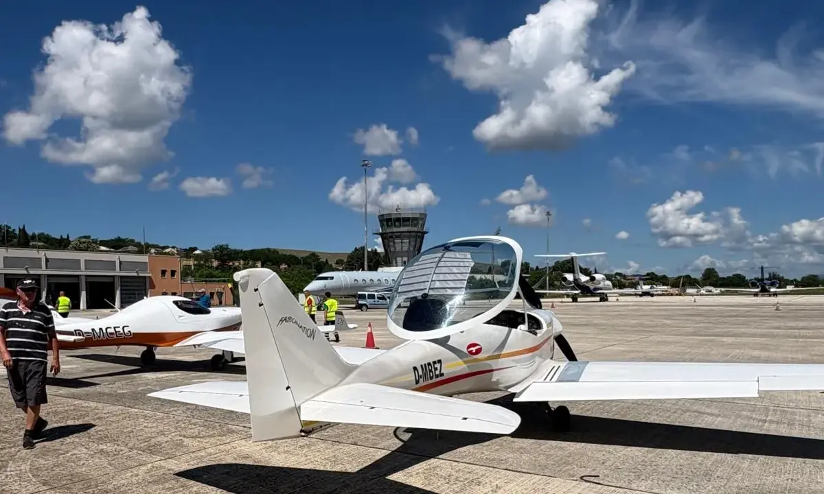 Zwei ultraleichtflugzeug modelle stehen auf dem Rollfeld. Im Hintergrund ein Kontrollturm und weitere Flugzeuge.
