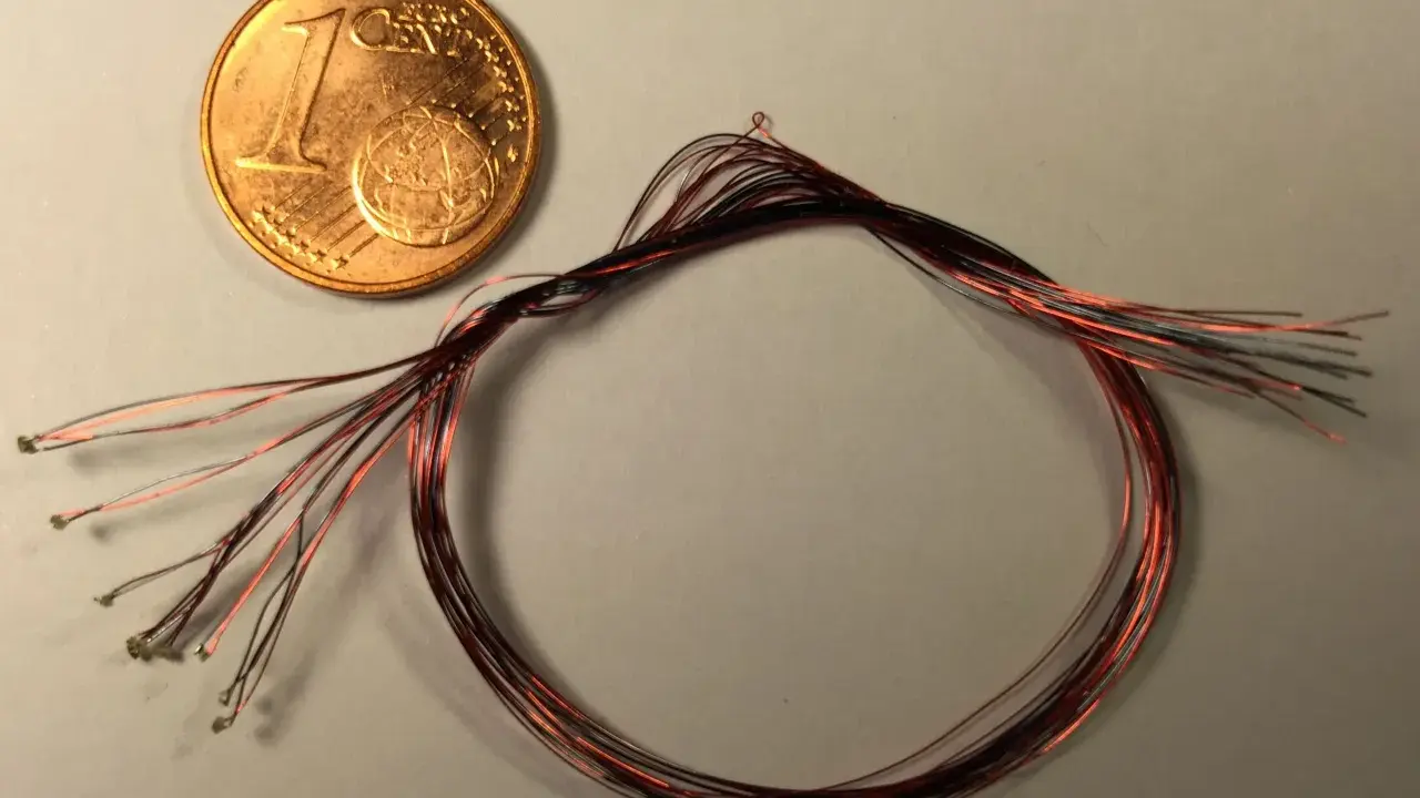 Ein-Cent-Münze neben einem Bündel dünner roter und schwarzer Kabel mit kleinen Lötpunkten.