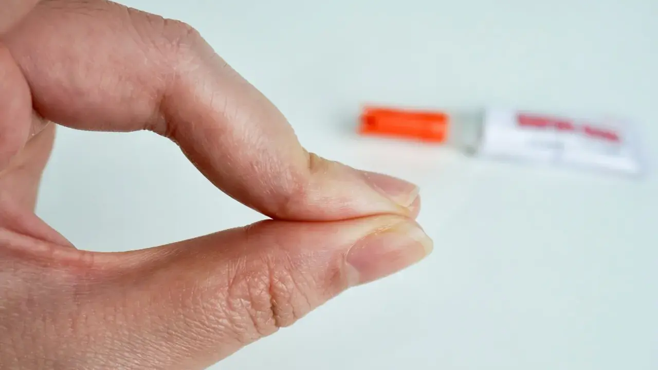 Fingerkuppen kleben zusammen. Ein Röhrchen mit debonder liegt unscharf im Hintergrund.