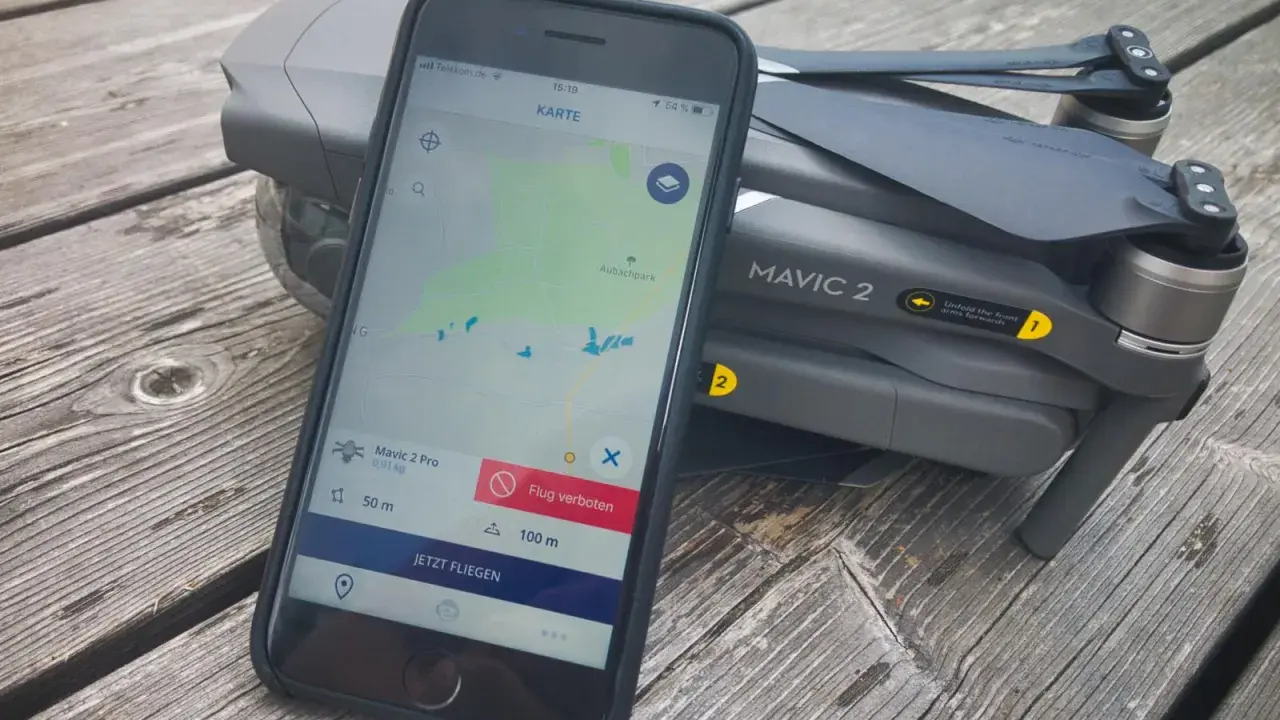 Eine Drohne liegt neben einem Smartphone, auf dem eine Drohnen-App mit Karte und Flugverboten angezeigt wird.