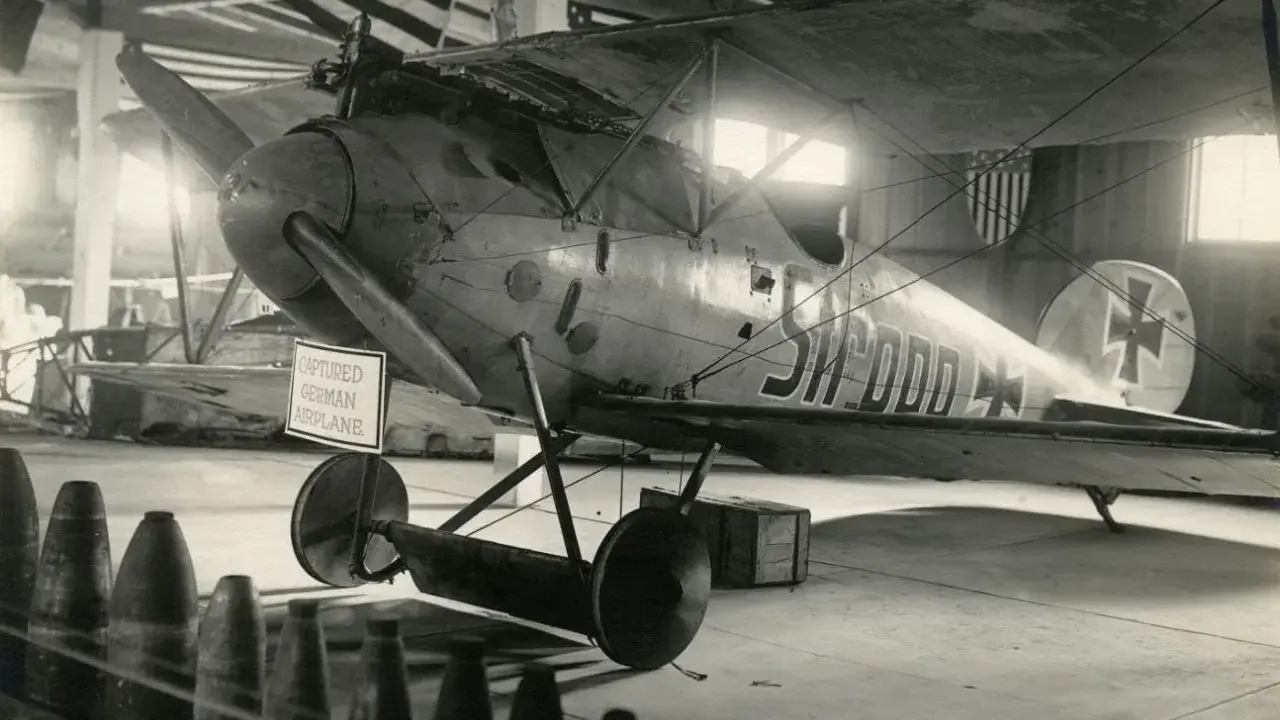 Gefangenes Albatros Flugzeug mit deutscher Kennung in einer Halle, hinter ihm US-Flaggen.