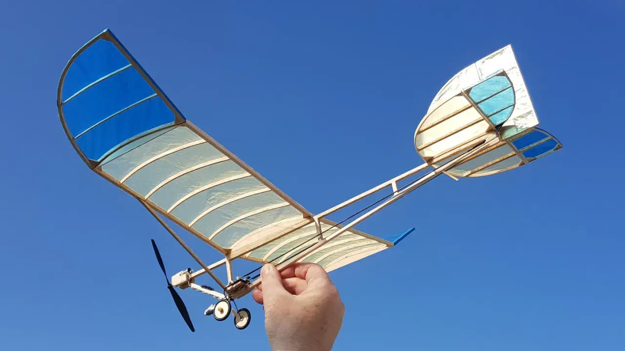 Ein handgefertigtes Modellflugzeug mit blau-weißen Flügeln, gehalten von einer Hand, bereit zum Flug. Ein echter slow flyer.