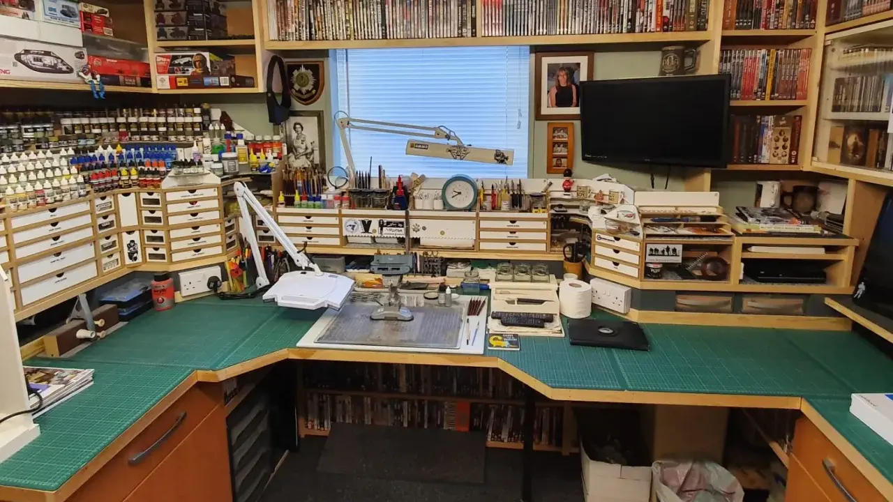 Ein Hobbyraum für **Plastikmodellbau**: Regale voller Modelle, Farben und Werkzeuge, eine Werkbank mit Schneidematte und Lupenlampe.