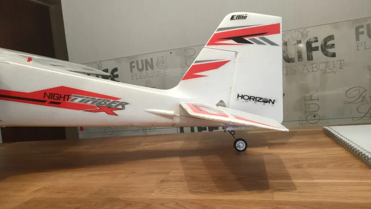 Modellflugzeug mit Aufschrift "NIGHT TIMBER" und "Eflite" Logo. Das Flugzeug steht auf einem Holztisch, bereit zum Flug.
