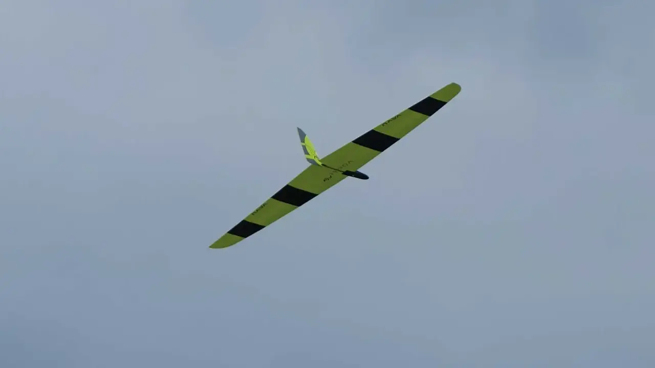 Ein gelb-schwarzes Flying Wing Segelflugzeug gleitet elegant durch den wolkenverhangenen Himmel.