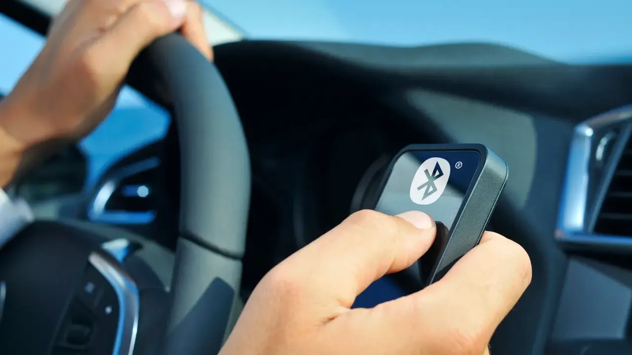 Fahrer hält ein Gerät mit Bluetooth-Symbol, während er das Lenkrad en 300 328 bedient.
