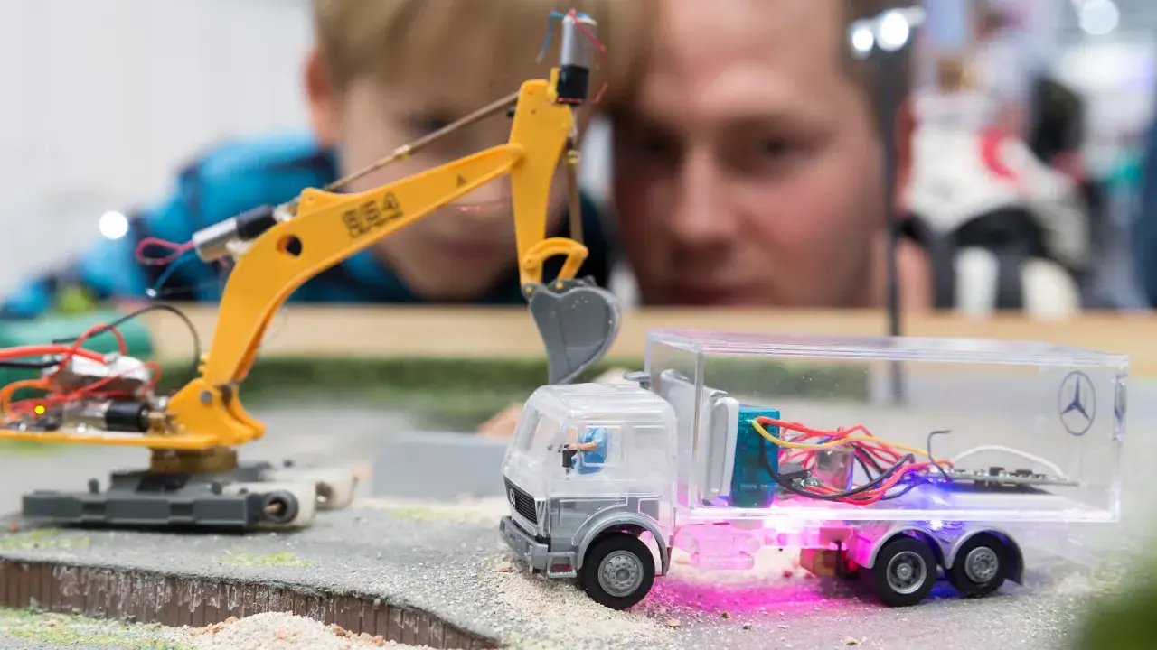 Faszination auf der **Hobby Messe Leipzig**: Ein Junge und ein Mann bestaunen eine ferngesteuerte Baustelle mit Bagger und LKW.