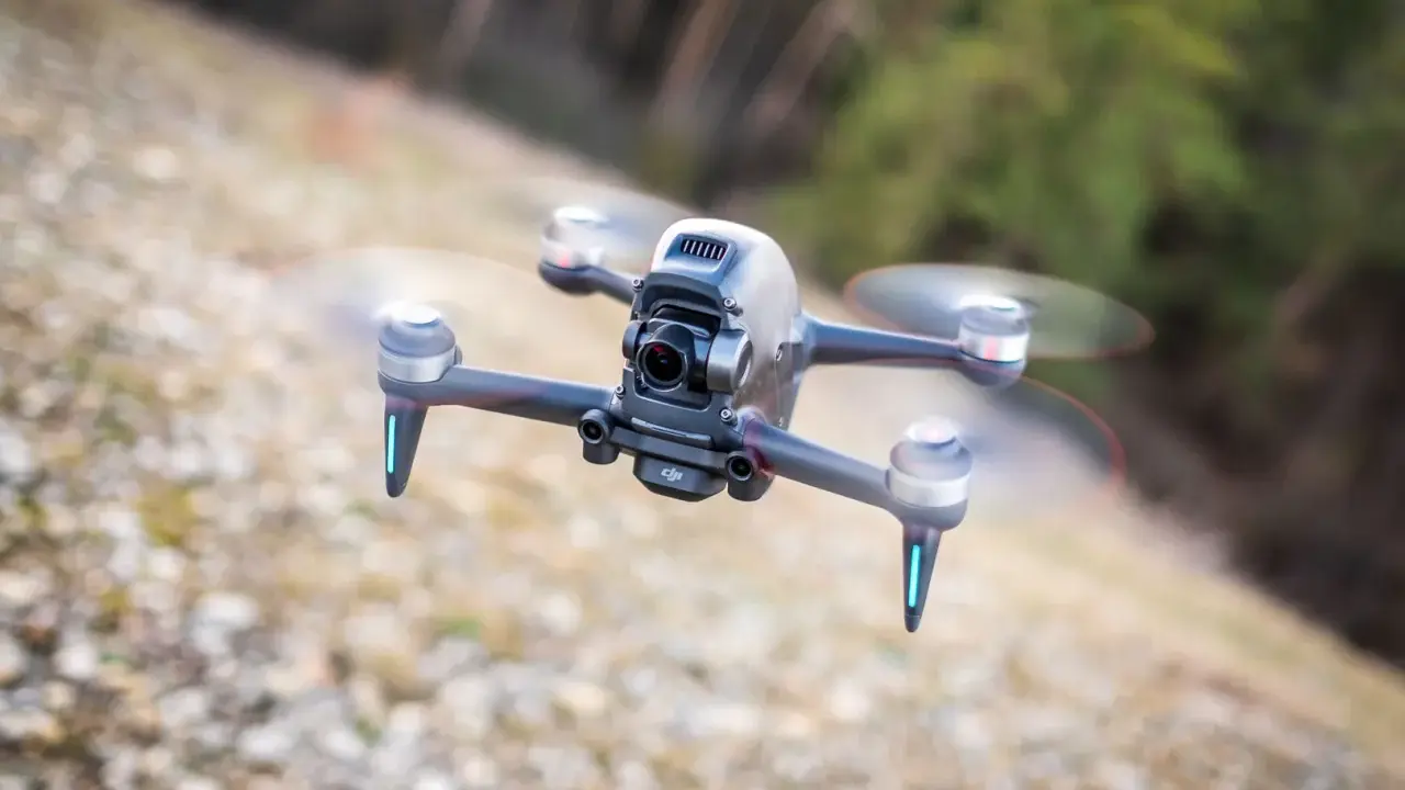 Eine FPV Drohne fliegt über steinigen Boden. Sie hat eine Kamera vorne und leuchtende blaue Lichter an den Armen.