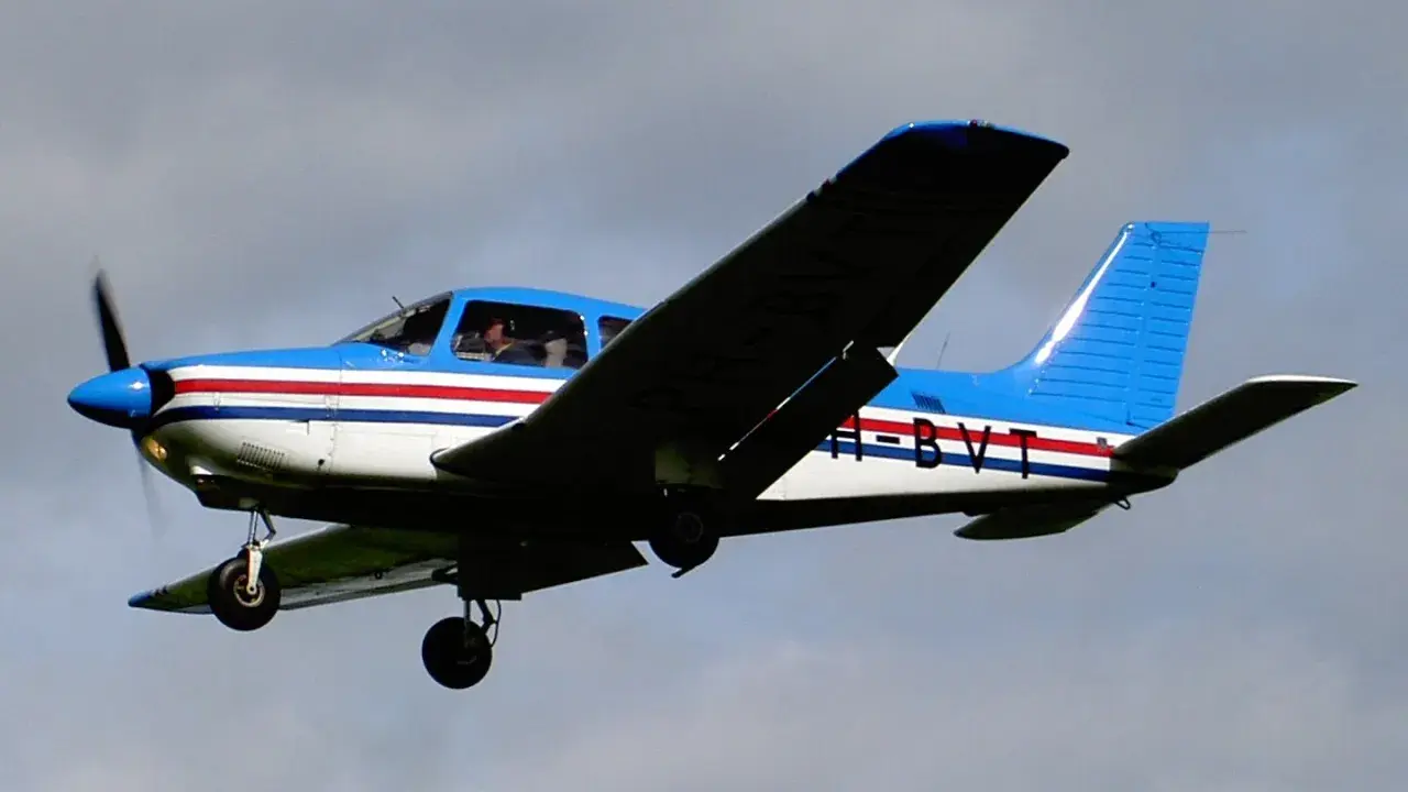 Blau-weiße Piper PA mit roten Streifen fliegt im Himmel.