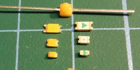 Mehrere kleine gelbe LEDs liegen auf einer grünen Schneidematte. Eine größere gelbe LED ist an einem Metallstift befestigt.
