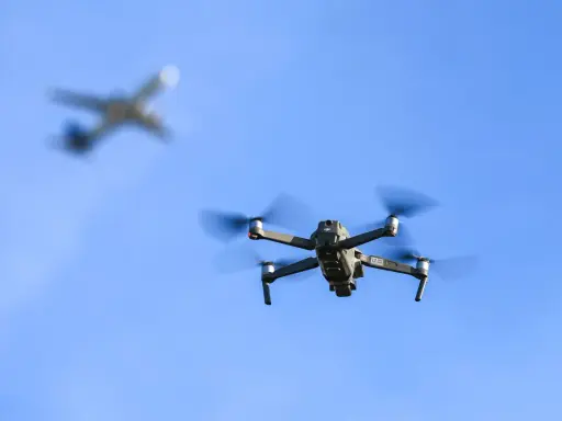 Ein moderner Drohne fliegt im Vordergrund, im Hintergrund ein unscharfes Flugzeug.