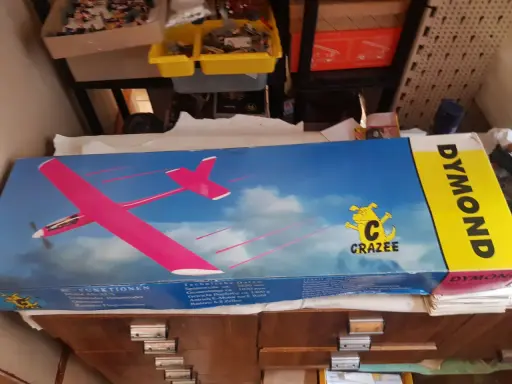 DYMOND RC-Flugzeug-Karton mit pinkem Modell. Ein gelber Streifen mit dem Schriftzug DYMOND.