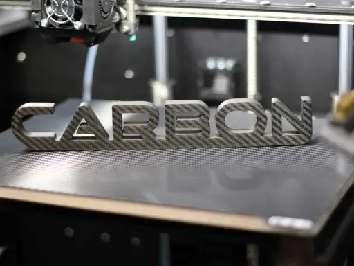 Ein 3D-Drucker fertigt das Wort "CARBON" aus einer Carbonplatte.