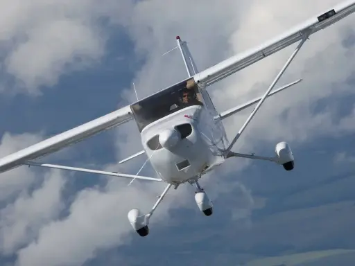Eine weiße Cessna Skyhawk fliegt durch bewölkten Himmel. Der Pilot blickt aus dem Cockpit.