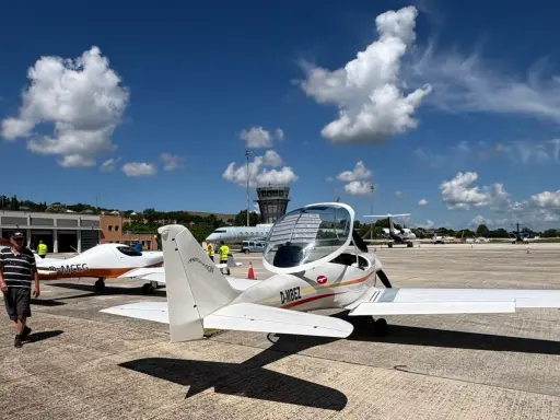 Zwei ultraleichtflugzeug modelle stehen auf dem Rollfeld. Im Hintergrund ein Kontrollturm und weitere Flugzeuge.