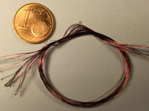 Ein-Cent-Münze neben einem Bündel dünner roter und schwarzer Kabel mit kleinen Lötpunkten.