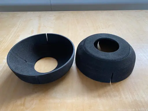 Zwei schwarze EPP-Platten, geformt wie Trichter und Zylinder, liegen auf einer Holzoberfläche.