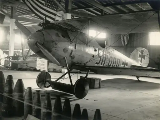 Gefangenes Albatros Flugzeug mit deutscher Kennung in einer Halle, hinter ihm US-Flaggen.
