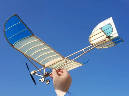 Ein handgefertigtes Modellflugzeug mit blau-weißen Flügeln, gehalten von einer Hand, bereit zum Flug. Ein echter slow flyer.