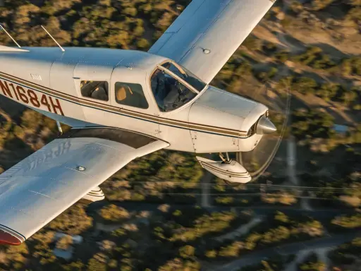 Eine Piper Cherokee 140 fliegt über eine bewaldete Landschaft.