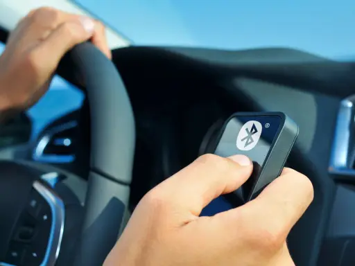 Fahrer hält ein Gerät mit Bluetooth-Symbol, während er das Lenkrad en 300 328 bedient.