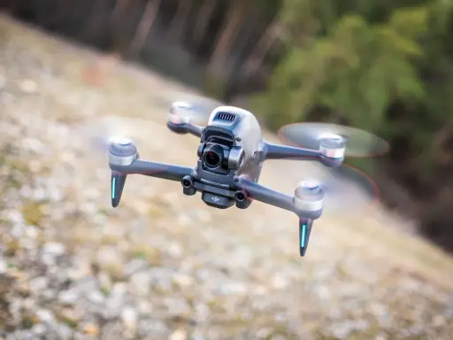Eine FPV Drohne fliegt über steinigen Boden. Sie hat eine Kamera vorne und leuchtende blaue Lichter an den Armen.