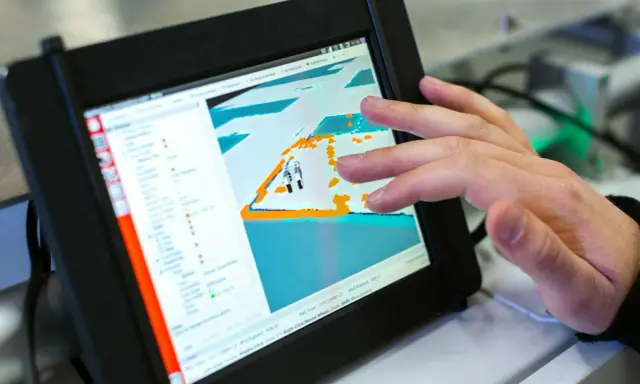 Ein Finger tippt auf ein Tablet, das eine 3D-Ansicht mit einem Roboter zeigt. Die dji app windows wird zur Steuerung genutzt.