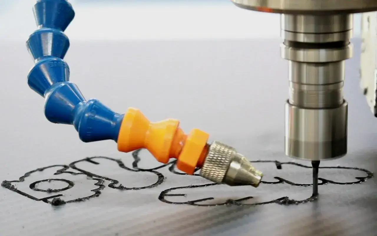 CNC-Fräser bearbeitet eine Carbonplatte, wobei ein Kühlmittelstrahl die Schnittkante kühlt.