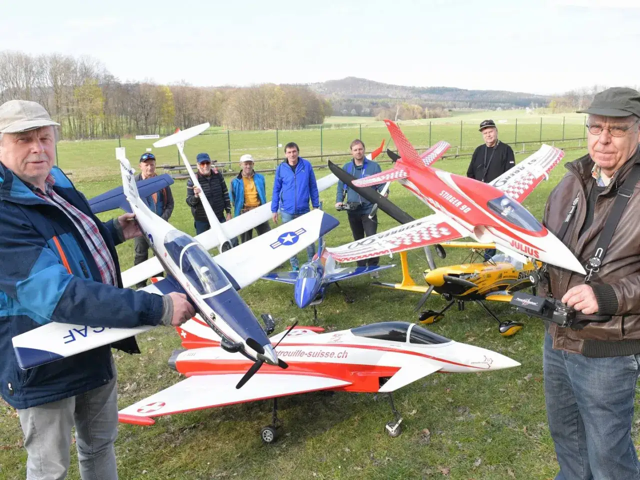 Männer präsentieren stolz ihre Modellflugzeuge auf einem Flugplatzfest.