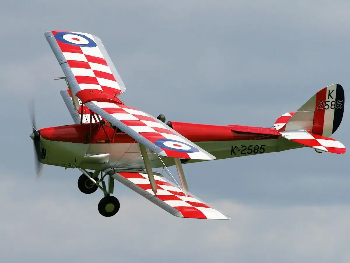 Ein roter Doppeldecker im Flug, der an einen Tiger Moth erinnert, mit roten und weißen Karos auf den Flügeln.