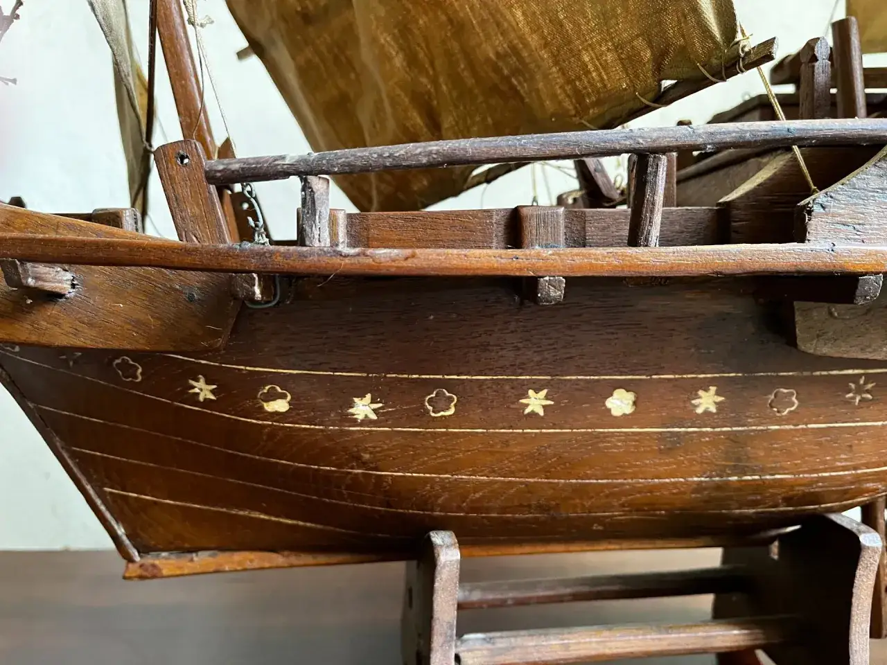 Detailaufnahme eines hölzernen Modells eines Dschunke Schiffs mit Segeln und Verzierungen am Rumpf.