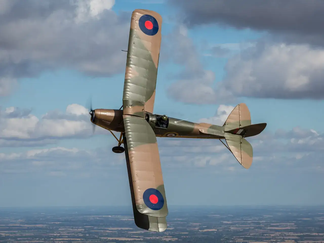 Ein Tiger Moth Flugzeug fliegt im Sonnenschein &uuml;ber eine Landschaft.