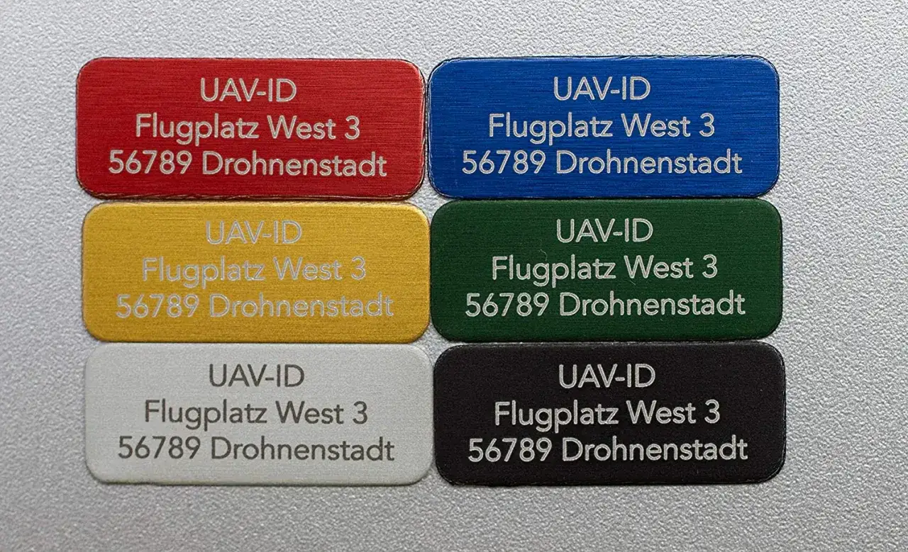 Sechs farbige Plaketten mit aufgedruckten Modellbau Kennzeichen: UAV-ID, Flugplatz West 3, 56789 Drohnenstadt.