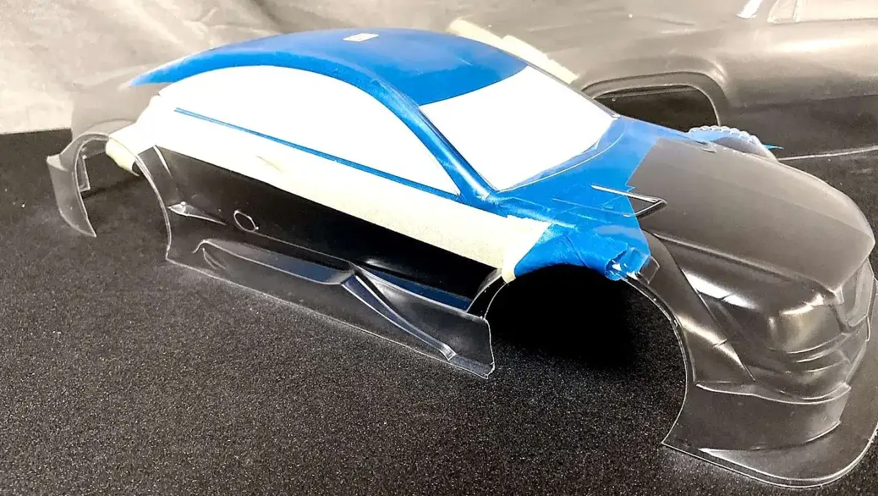 RC-Karosserie wird für das Lackieren vorbereitet. Blaue und weiße Farbe sind aufgetragen, Fenster sind abgeklebt.