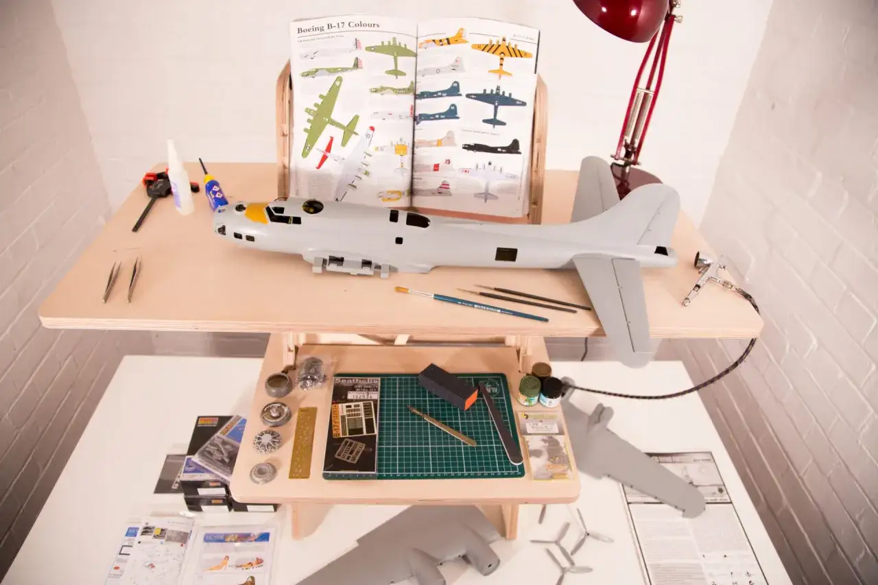 Detailreicher Plastikmodellbau eines Flugzeugs, mit Werkzeugen, Farben und einem Referenzbuch.