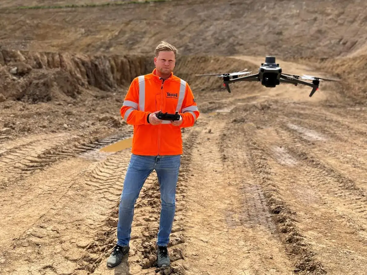 Mann in Warnweste steuert Drohne für präzise Drohnen Maps auf Baustelle.