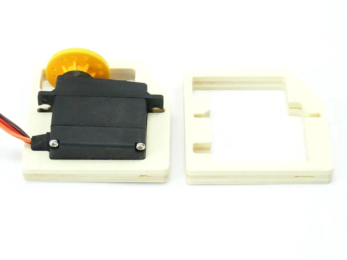 Ein Servomotor mit gelbem Rad auf Holz montiert, daneben ein Holzrahmen. Ein kleiner, präziser dymond-Mechanismus.