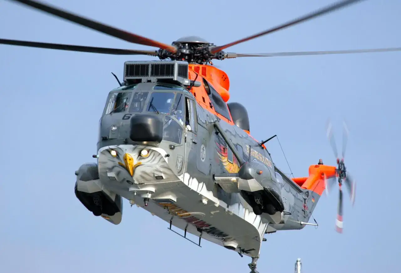 Ein Sea King Hubschrauber mit Adlerbemalung fliegt vor blauem Himmel.