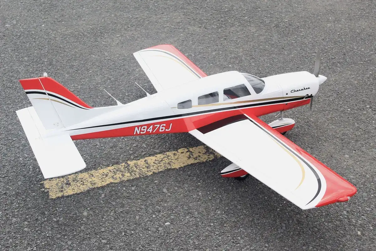 Ein weißes Piper Flugzeug mit roten Akzenten und der Kennung N9476J steht auf Asphalt.