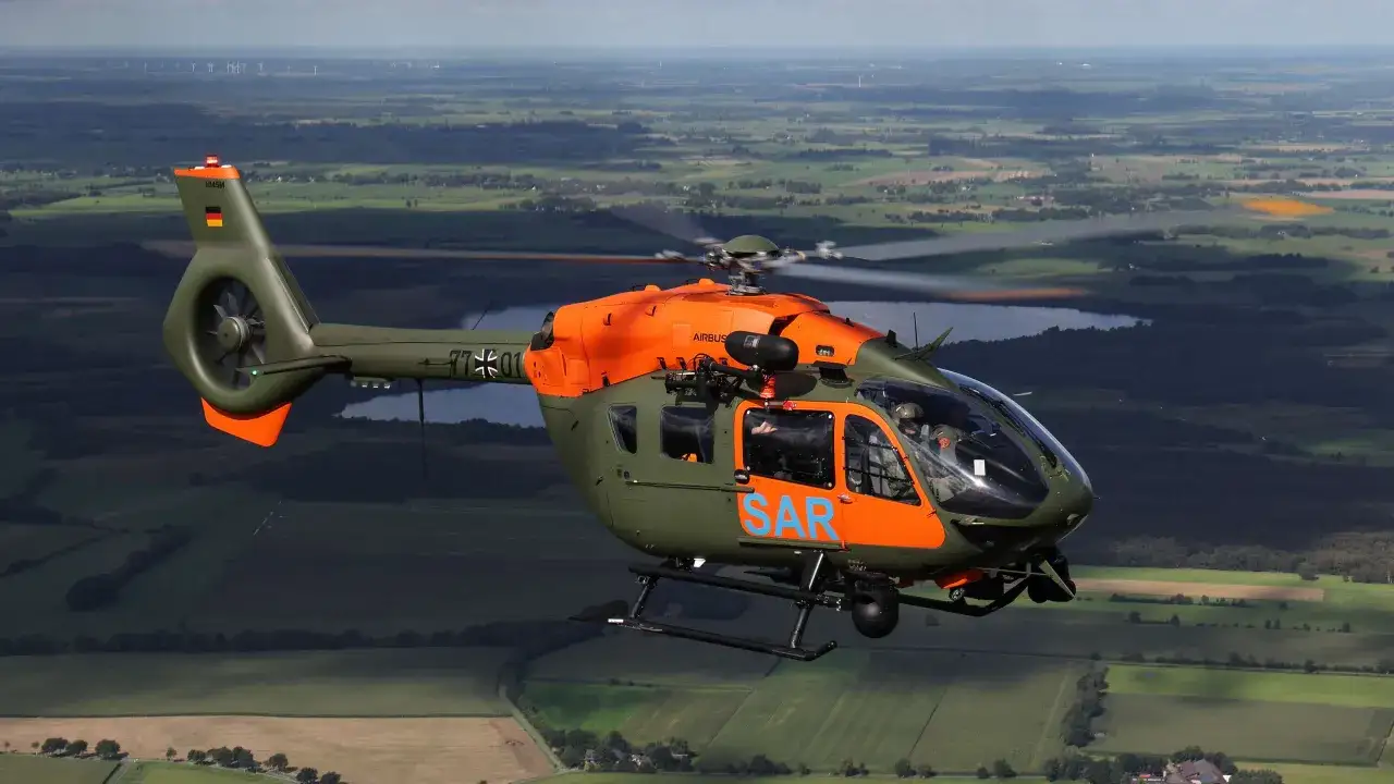 Ein deutscher SAR-Hubschrauber fliegt über eine grüne Landschaft.