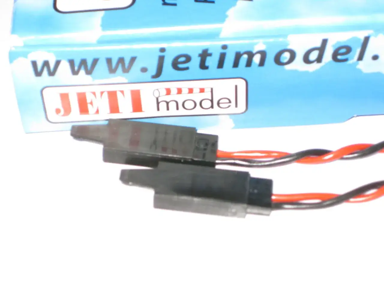 Zwei schwarze Stecker mit roten und schwarzen Kabeln, Teil eines jeti bec Systems, liegen vor einer Verpackung mit dem Logo 