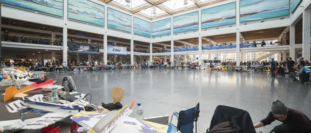 Menschen bestaunen Modellflugzeuge in einer großen Halle. Die Faszination Modellbau ist überall spürbar, während die Besucher die detailreichen Modelle betrachten.