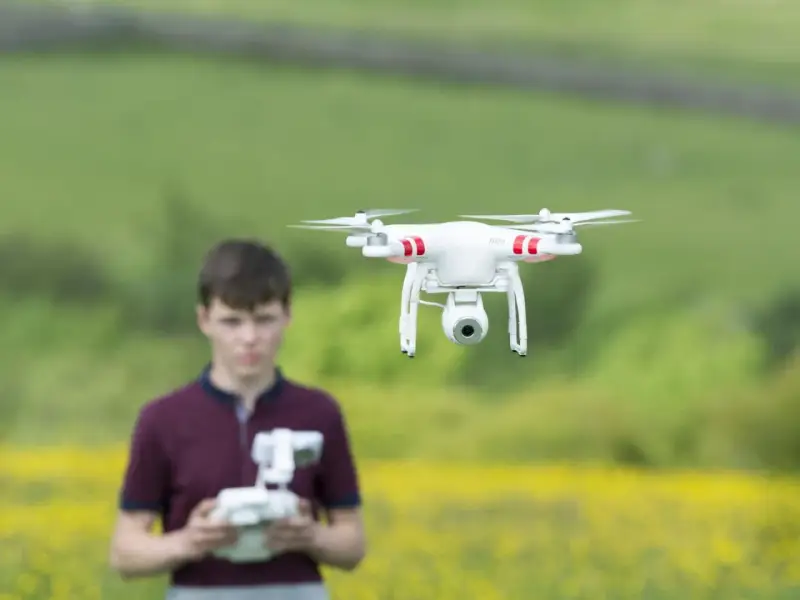 Ein Junge steuert eine Drohne in Litauen. Die Drohne schwebt über einem Feld mit gelben Blumen.